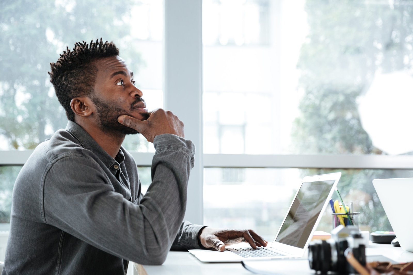 Picture of handsome thinking serious young man sitting in office coworking. Looking aside using laptop computer.